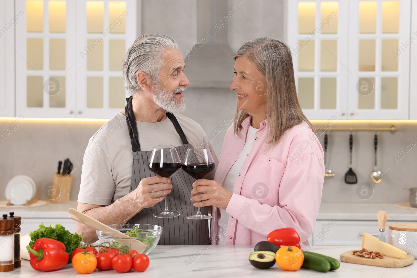 Photo of Happy affectionate senior couple with glasses of wine in kitchen