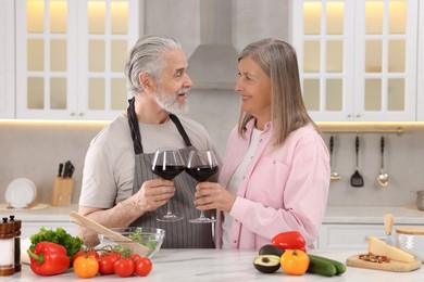 Happy affectionate senior couple with glasses of wine in kitchen