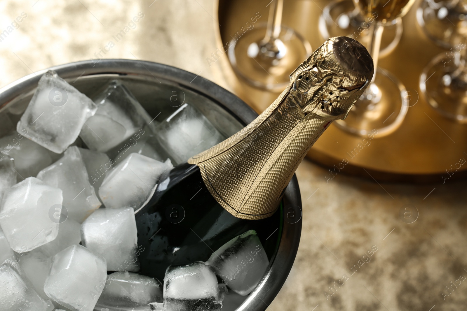 Photo of Bottle of champagne in bucket with ice cubes on table, closeup