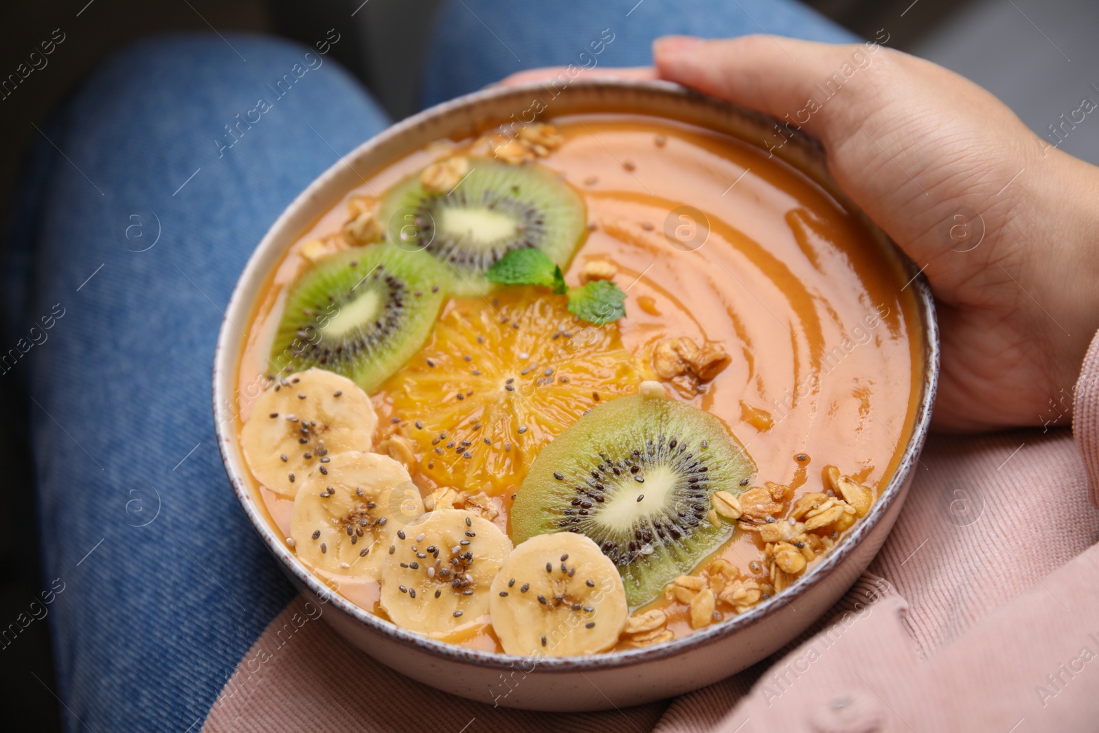 Photo of Woman holding bowl of delicious fruit smoothie with fresh banana, kiwi slices and granola, closeup