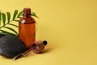 Photo of Bottleface serum, spa stones and leaf on yellow background. Space for text