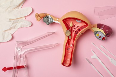 Photo of Gynecological examination kit and anatomical uterus model on pink background, flat lay