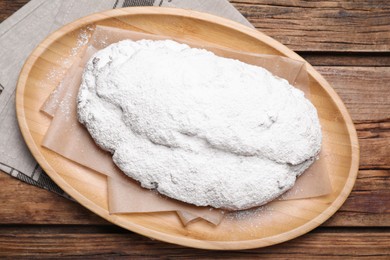Photo of Plate of delicious Stollen sprinkled with powdered sugar on wooden table, top view