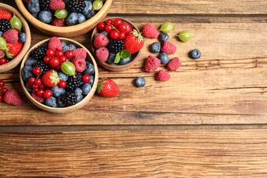 Mix of ripe berries on wooden table, flat lay. Space for text