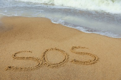 Photo of Message SOS drawn on sand near sea