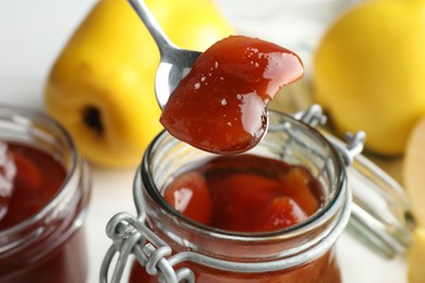 Taking tasty homemade quince jam from jar on blurred background, closeup