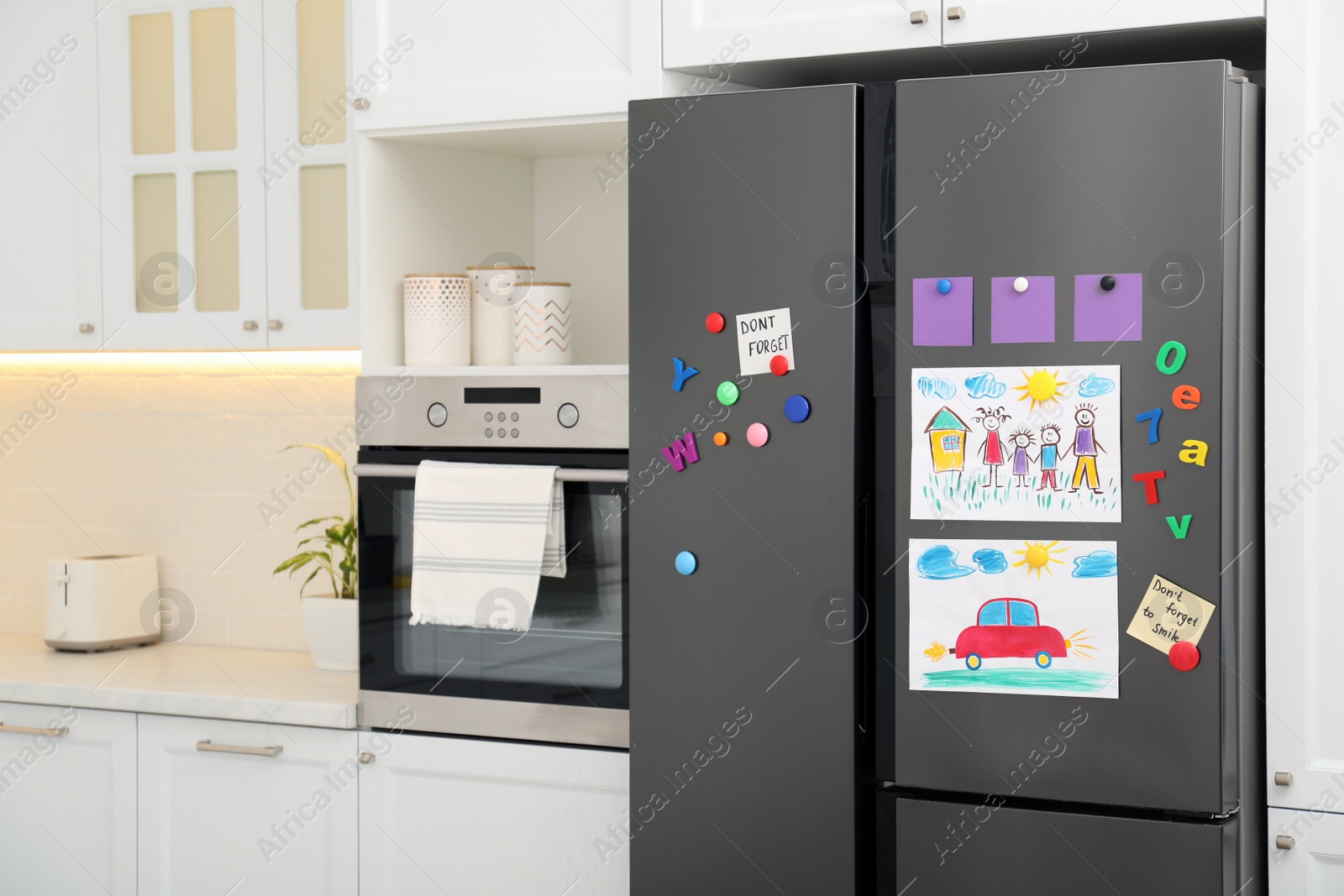 Photo of Modern refrigerator with child's drawings, notes and magnets in kitchen. Space for text