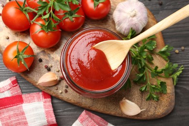 Photo of Tasty ketchup, fresh tomatoes, parsley and spices on grey wooden table, flat lay