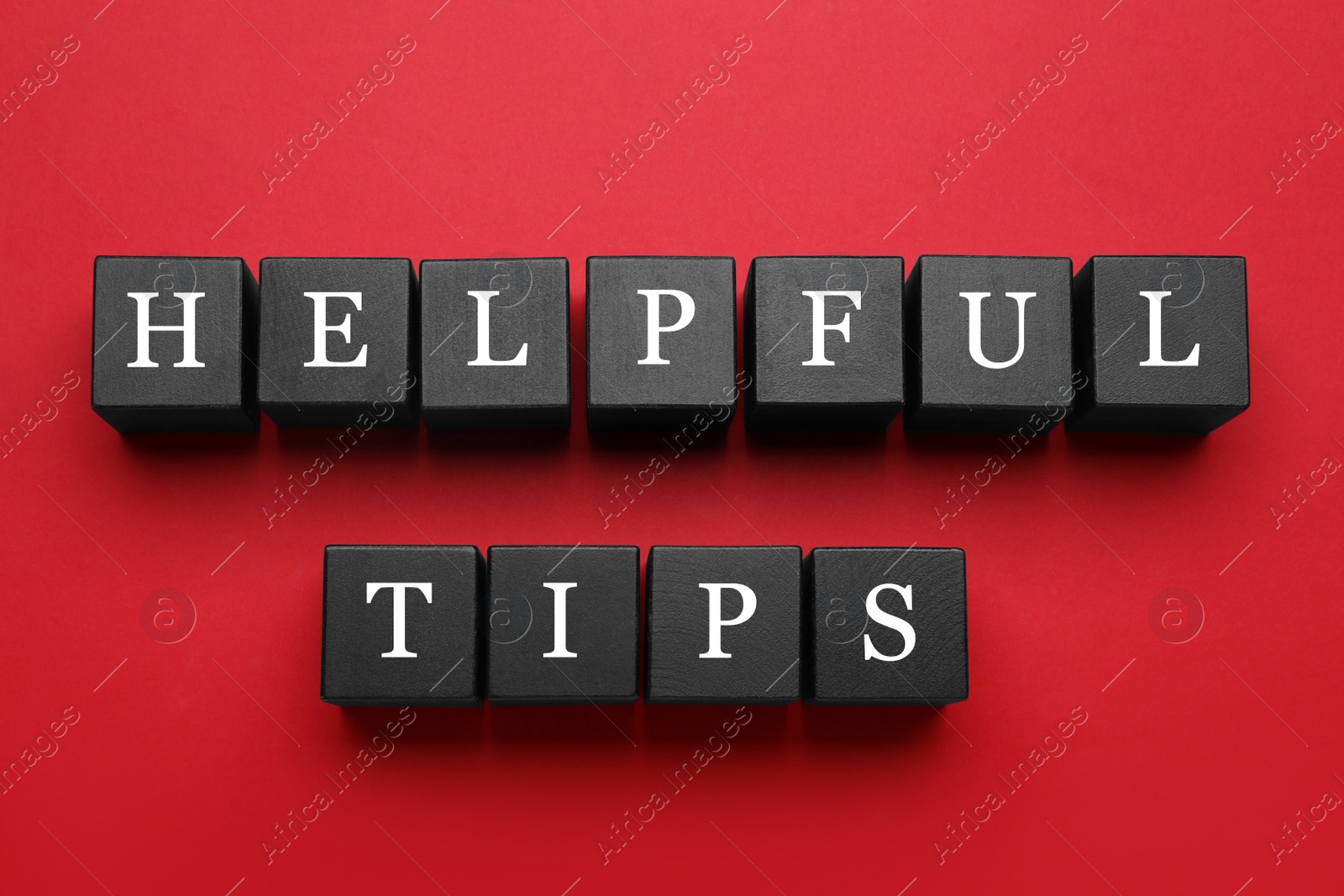 Photo of Phrase Helpful Tips made of black cubes with letters on red background, top view