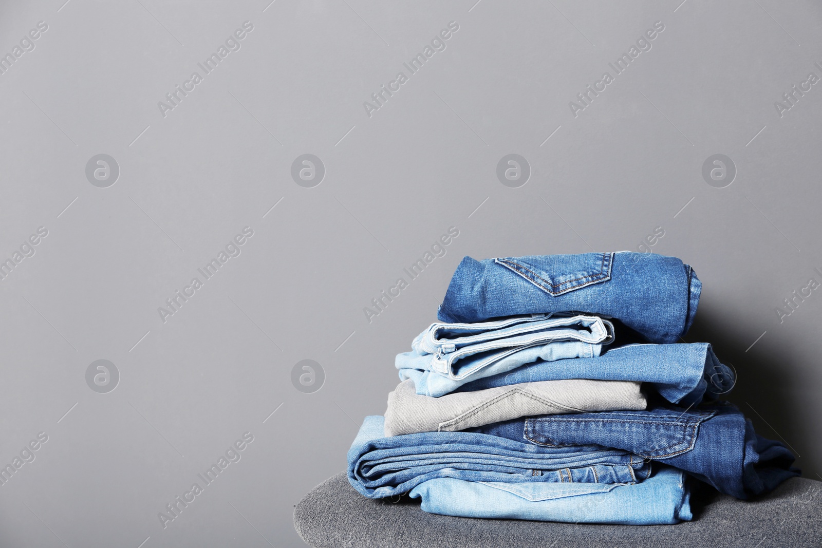 Photo of Stack of different jeans on stool against gray background. Space for text