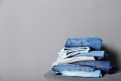 Photo of Stack of different jeans on stool against gray background. Space for text