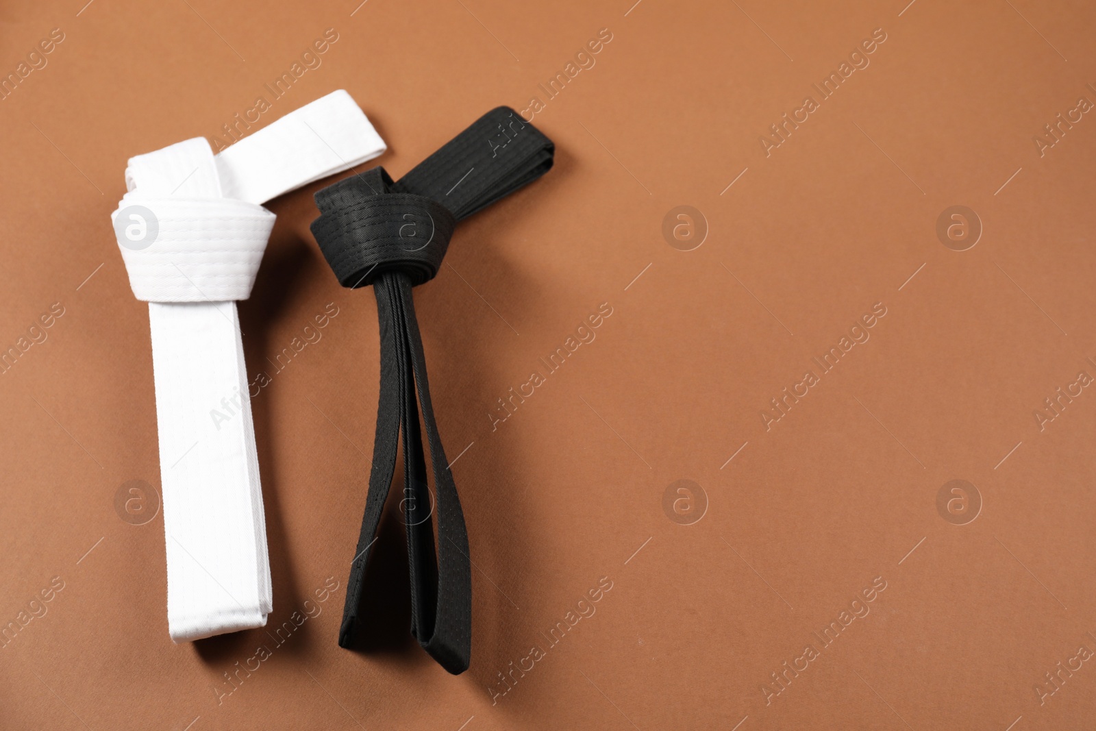 Photo of White and black karate belts on brown background, flat lay. Space for text