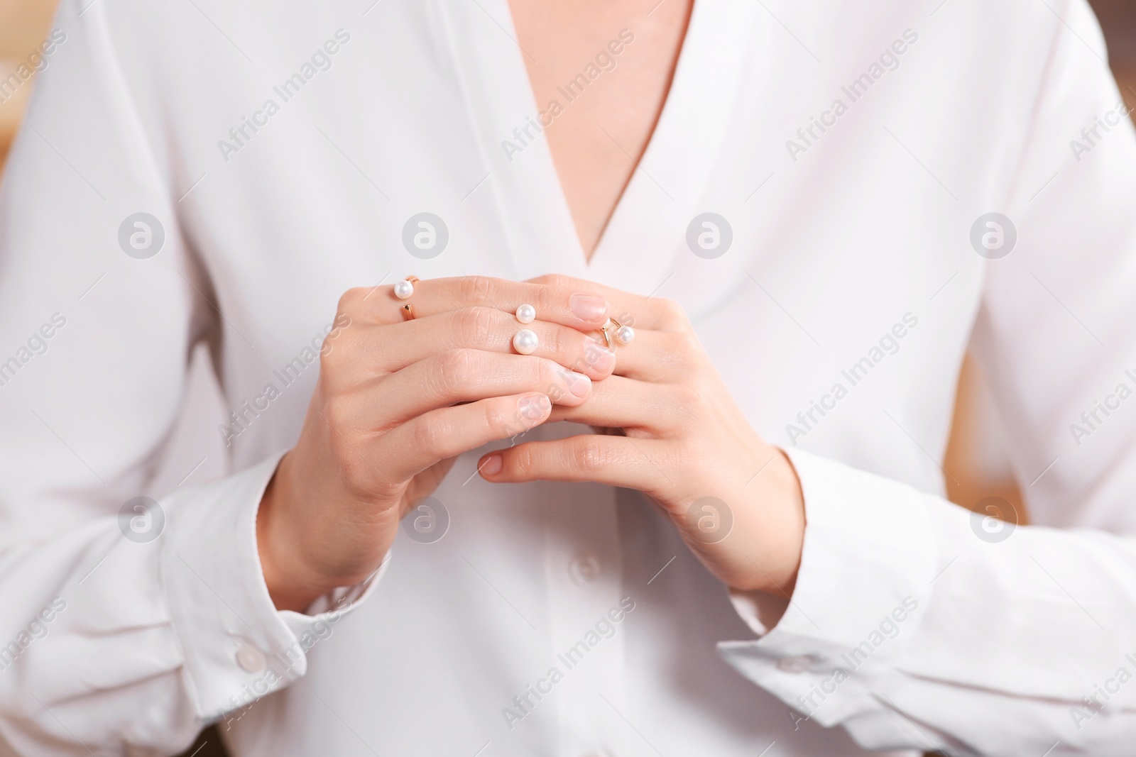 Photo of Young woman trying on elegant rings with pearls indoors, closeup