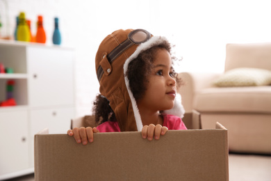 Cute African American child playing with cardboard box at home