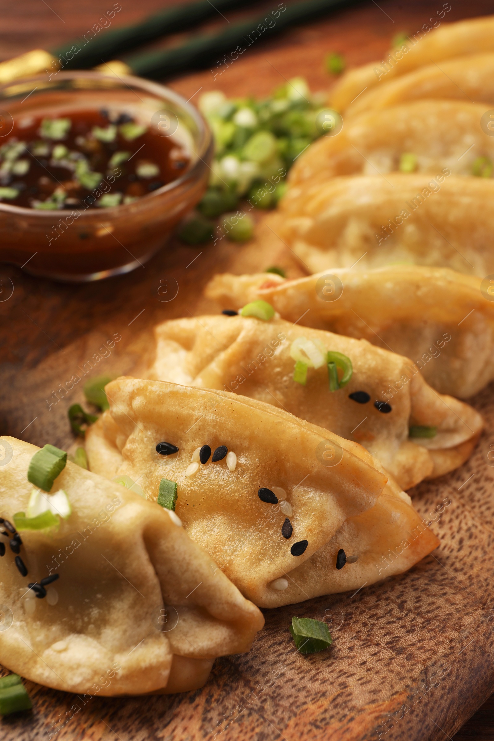 Photo of Delicious gyoza (asian dumplings) with sesame seeds and green onions on board, closeup