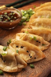 Photo of Delicious gyoza (asian dumplings) with sesame seeds and green onions on board, closeup