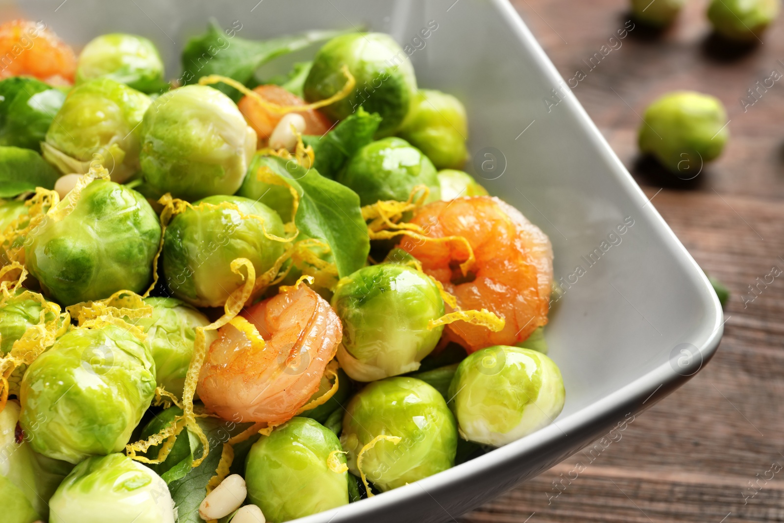 Photo of Bowl of delicious salad with Brussels sprouts and shrimps on table, closeup