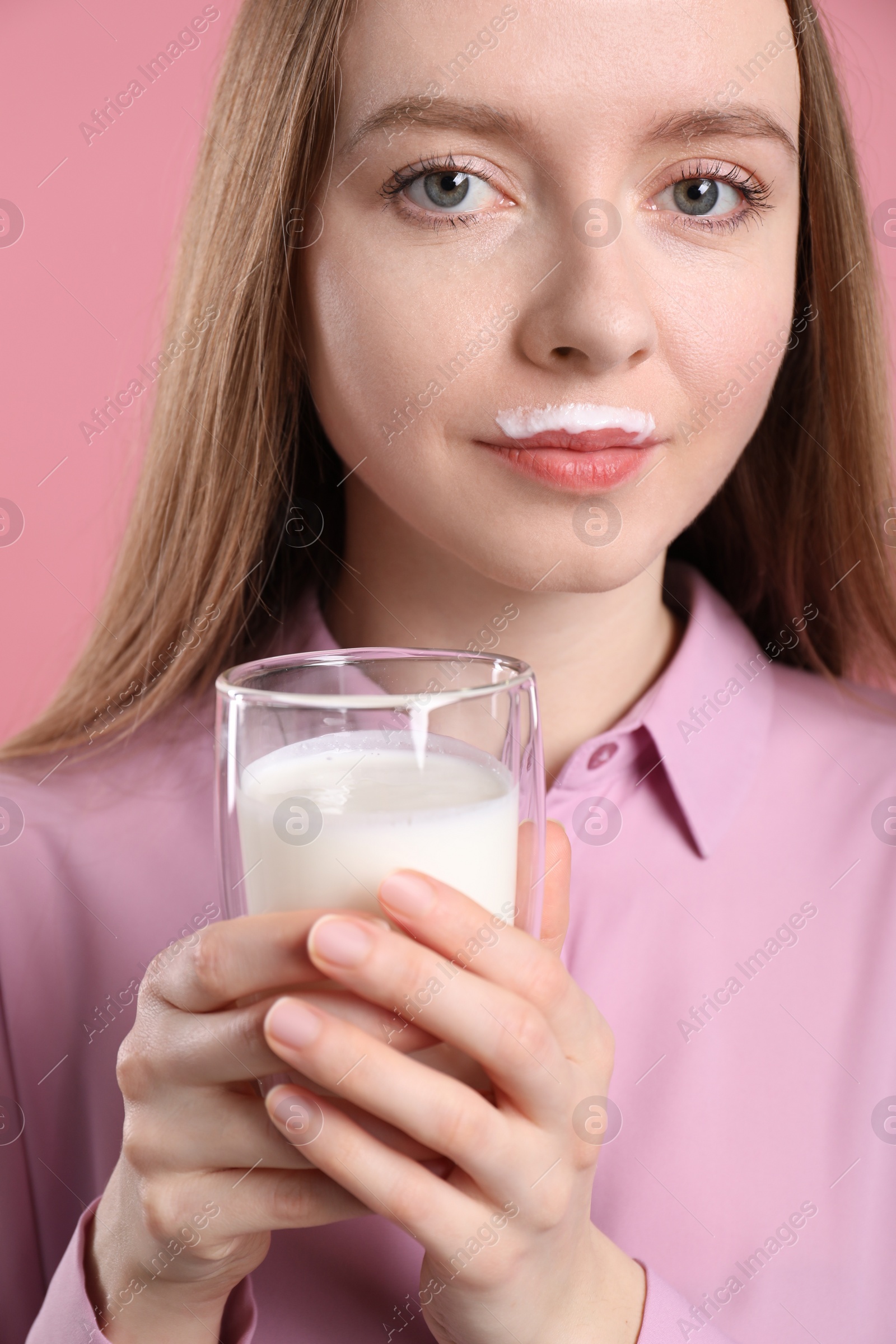 Photo of Cute woman with milk mustache holding glass of tasty dairy drink on pink background