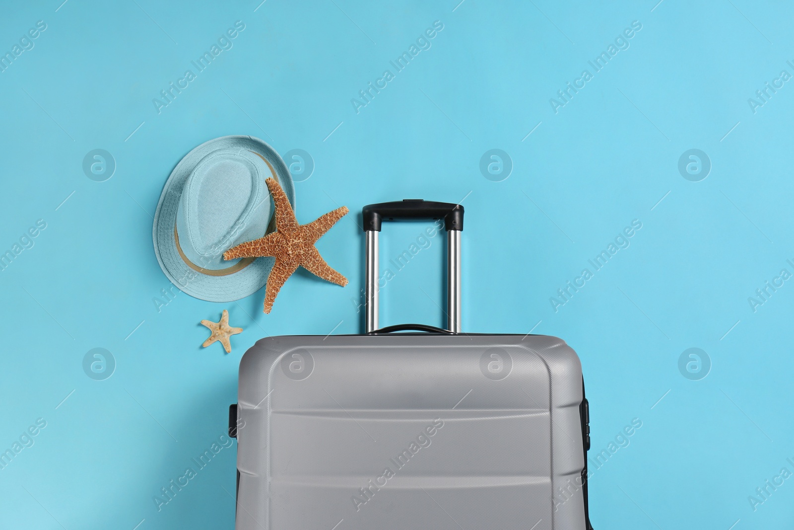 Photo of Stylish suitcase, sea stars and hat on color background, top view