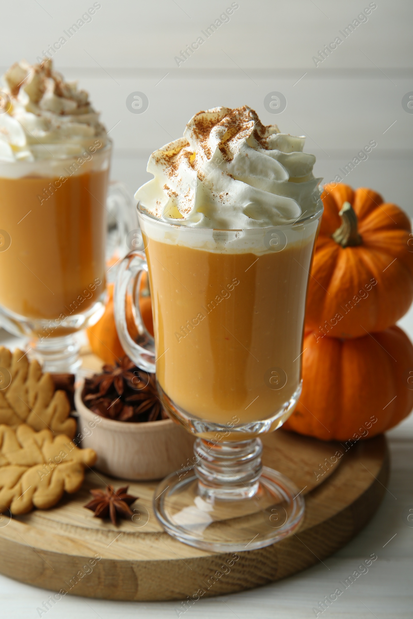 Photo of Tasty pumpkin latte with whipped cream in glasses, spices and cookies on white wooden table, closeup