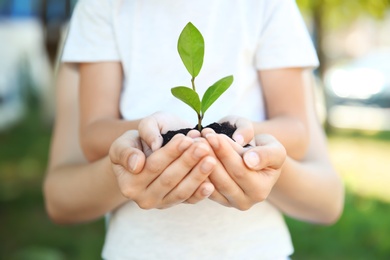 Photo of Woman and her child holding soil with green plant in hands on blurred background. Family concept