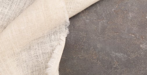 Photo of Beige burlap fabric on grey textured table, top view. Space for text