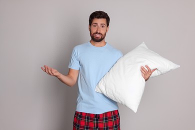 Emotional handsome man with pillow on light grey background