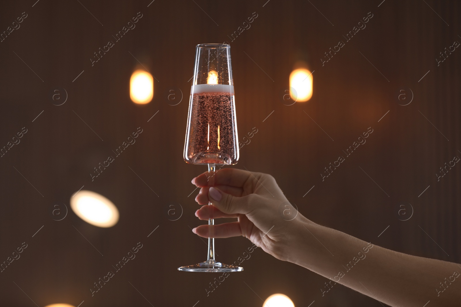 Photo of Woman holding glass of champagne against blurred lights, closeup