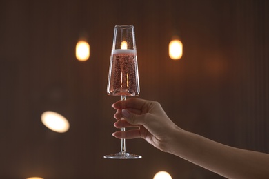 Photo of Woman holding glass of champagne against blurred lights, closeup