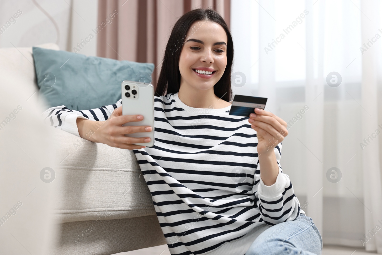 Photo of Happy young woman with credit card using smartphone for shopping online at home