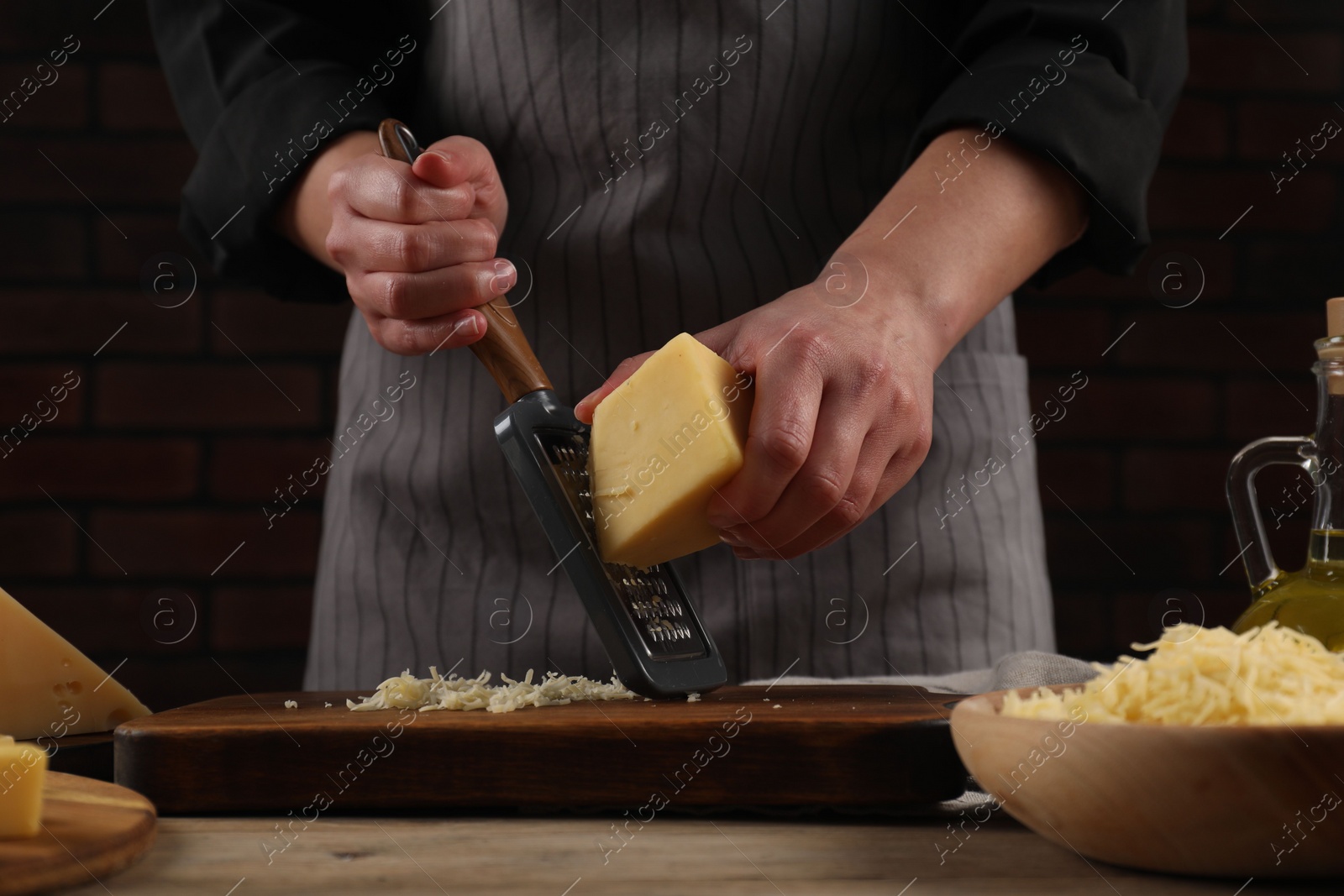 Photo of Woman grating cheese at wooden table, closeup