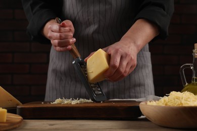 Woman grating cheese at wooden table, closeup