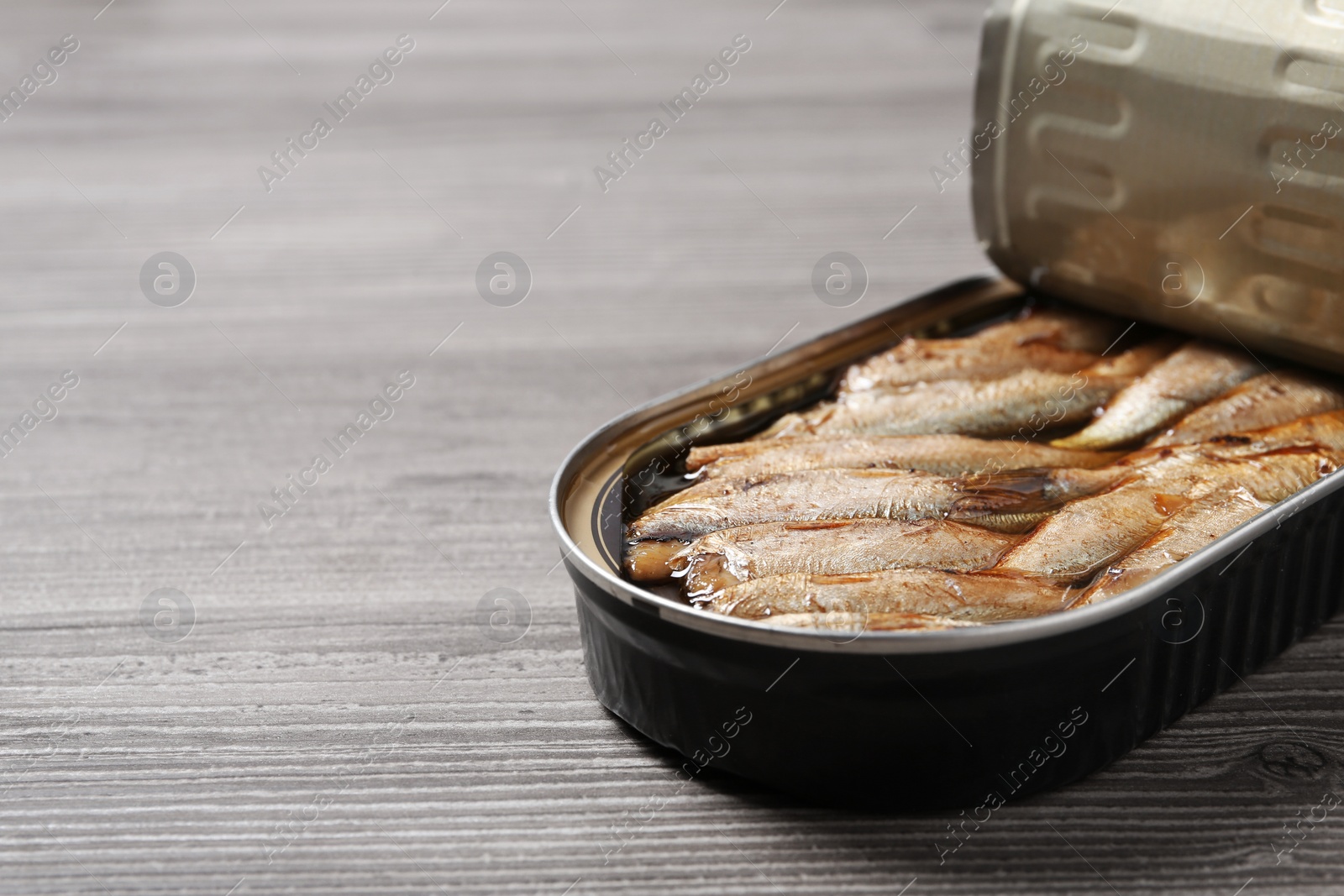 Photo of Open tin can with sprats on wooden table, closeup. Space for text