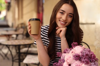 Beautiful woman with bouquet of spring flowers and coffee in outdoor cafe, space for text