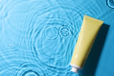 Photo of Tube with moisturizing cream in water on light blue background, top view. Space for text