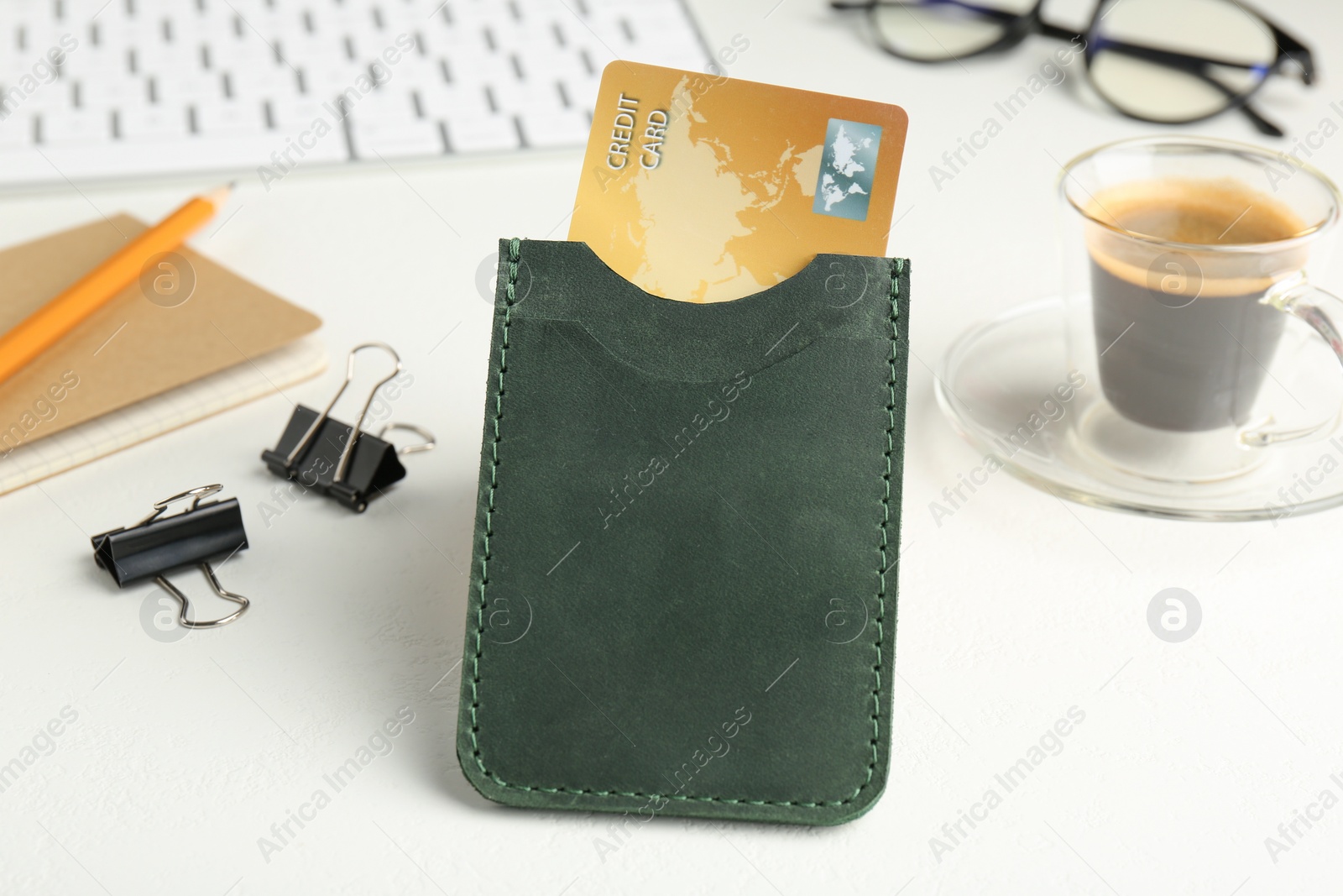 Photo of Leather card holder with credit card, stationery, coffee and keyboard on white table