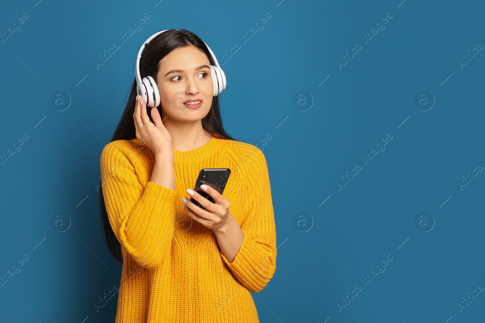 Photo of Young woman listening to audiobook on blue background. Space for text