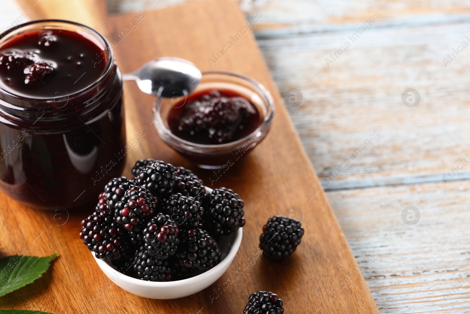 Photo of Fresh ripe blackberries and tasty jam on rustic wooden table. Space for text