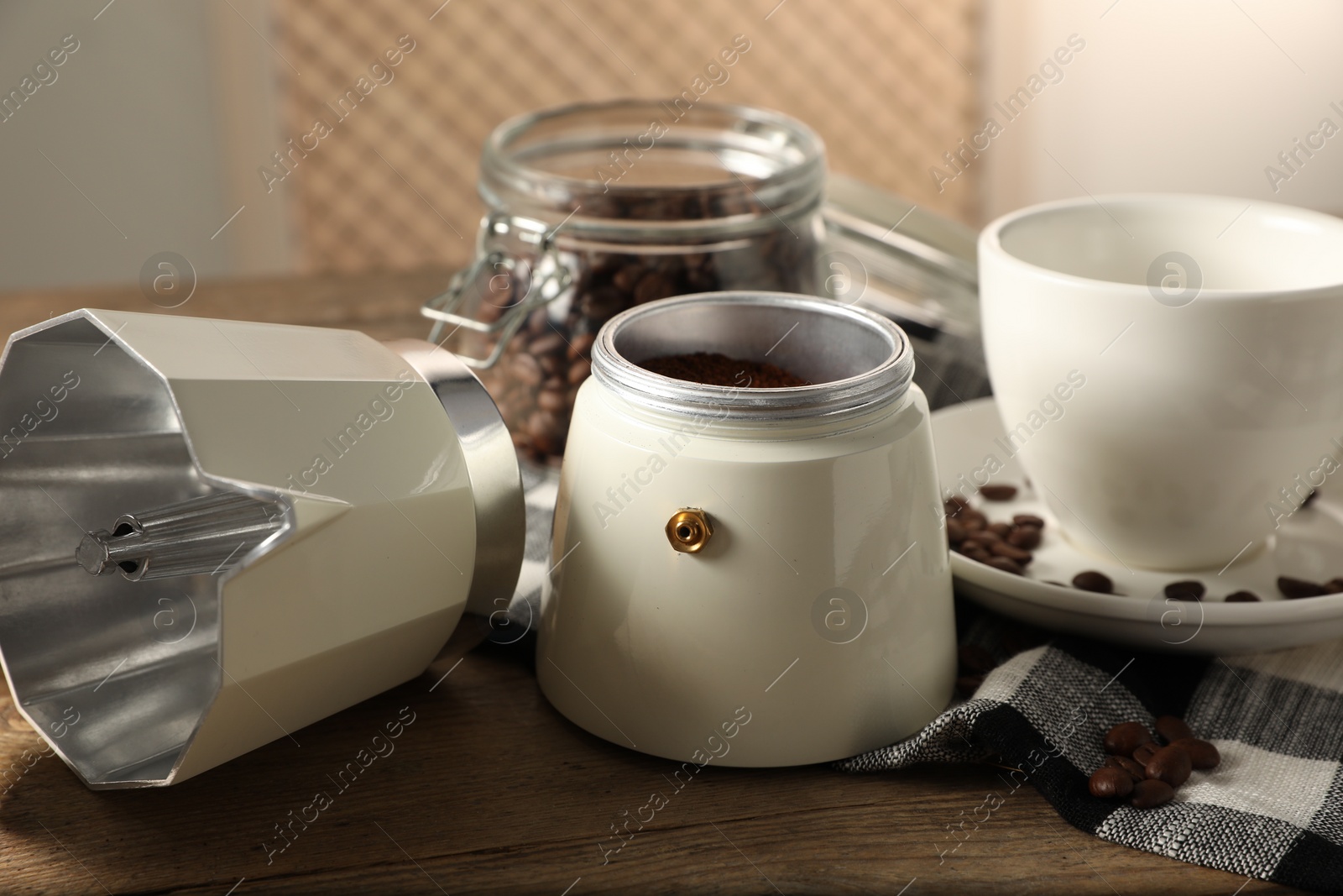 Photo of Moka pot with ground coffee and cup on wooden table indoors