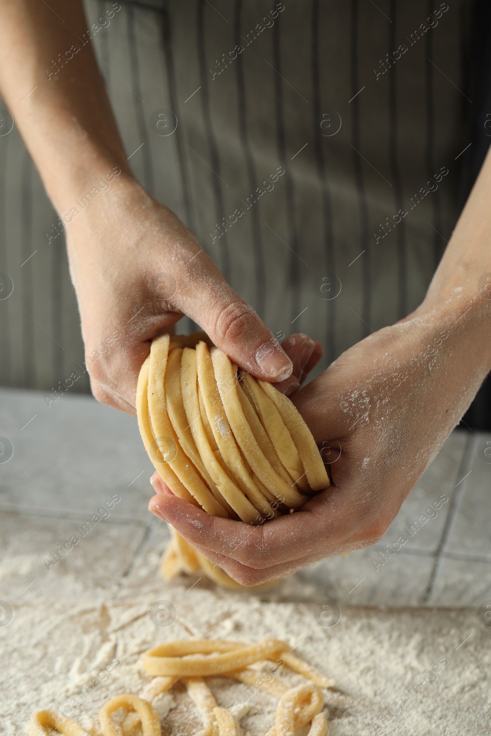 Photo of Woman with homemade pasta at light tiled table, closeup