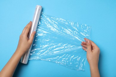 Photo of Woman with roll of stretch wrap on light blue background, top view