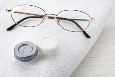 Case with contact lenses, glasses and towel on white wooden table, closeup