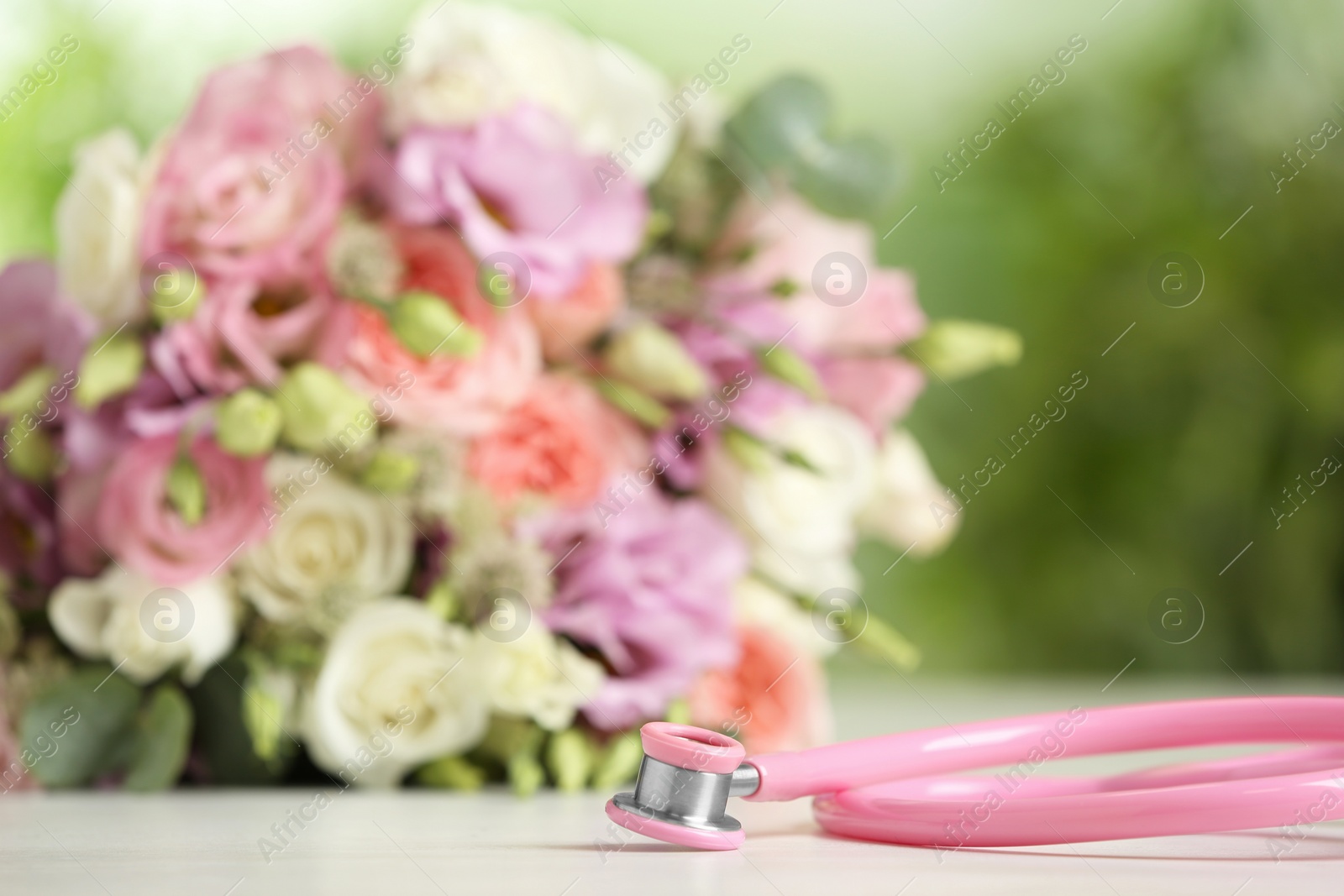 Photo of Stethoscope and flowers on white table against blurred background, space for text. World health day