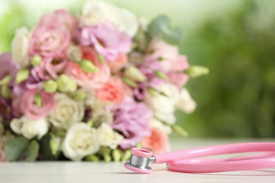 Photo of Stethoscope and flowers on white table against blurred background, space for text. World health day