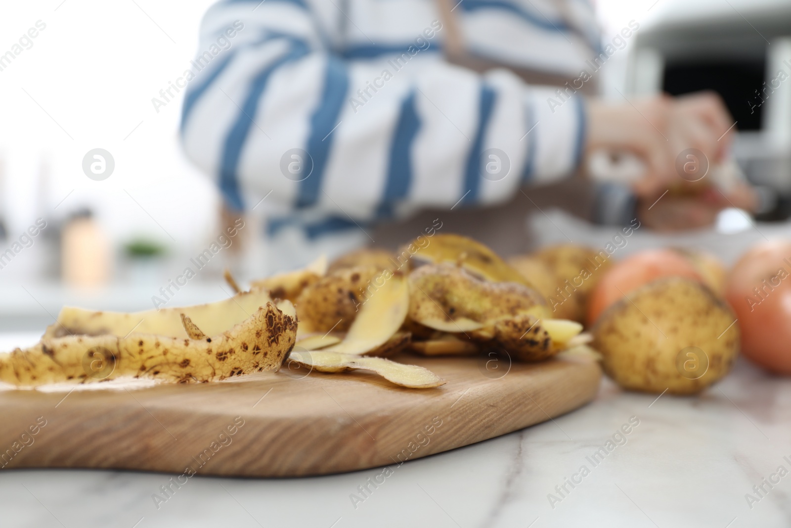 Photo of Woman peeling fresh potato at white marble table indoors, focus on peels