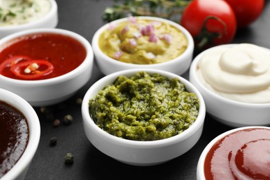 Different tasty sauces in bowls on black table, closeup