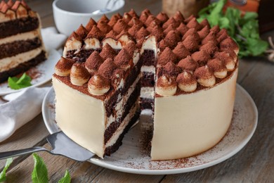 Photo of Delicious tiramisu cake with mint leaves and server on wooden table, closeup