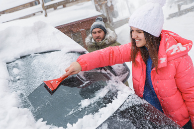 Photo of Young couple cleaning snow from car outdoors on winter day