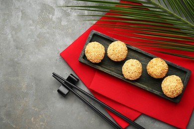 Photo of Delicious sesame balls, green leaf and chopsticks on grey table, flat lay. Space for text