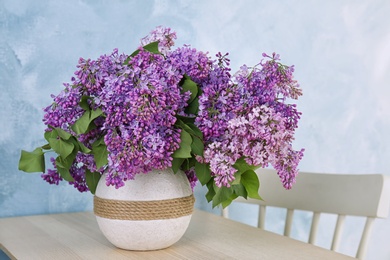 Photo of Vase with beautiful blossoming lilac on table against color background. Spring flowers